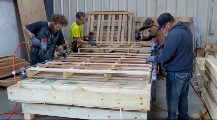 four workers at a hand table using nail guns to nail pallets