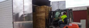 A photo a stacks of pallet carried by a forklift into a heat treatment system