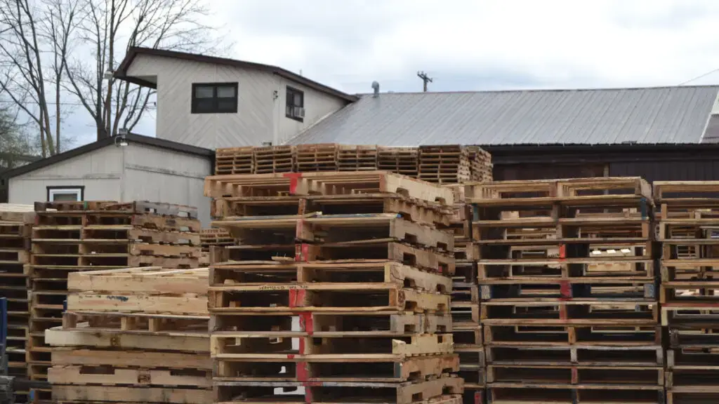 Stacks of wooden palletes sit outside a warehouse