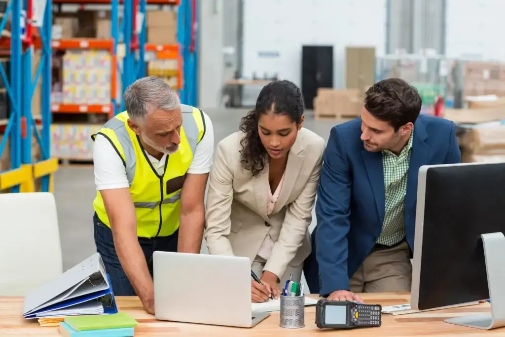 Three warehouse team members reviewing real-time pallet inventory data on a pallet tracking system dashboard