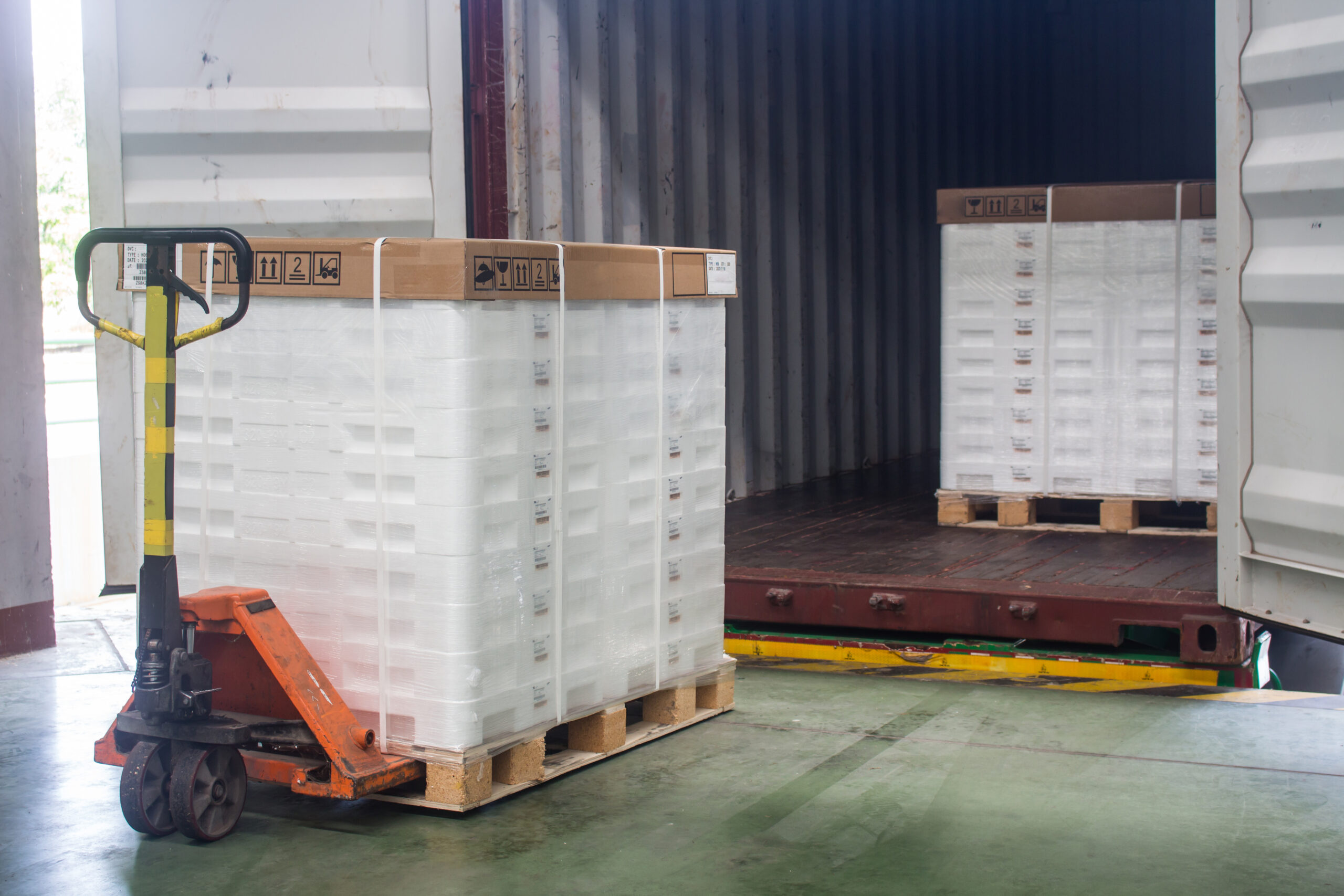 Palletized plastic packaging products secured on standardized pallets at a shipping dock, demonstrating a unified packaging procurement strategy