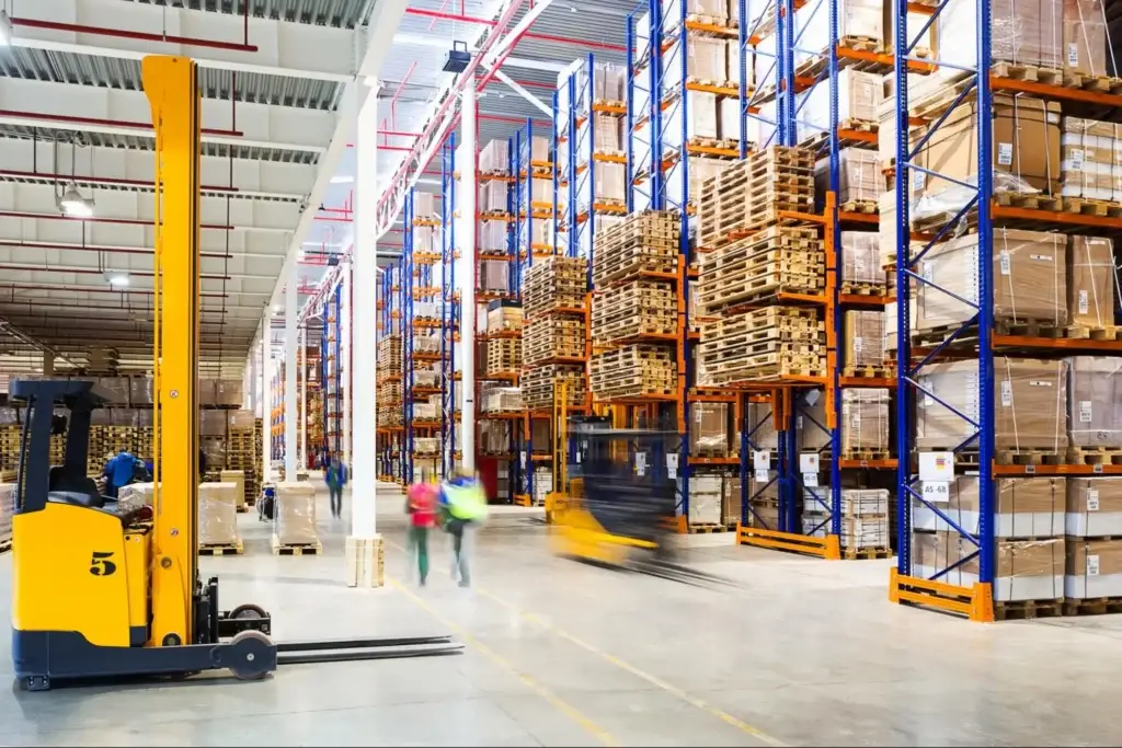 Wood pallets stacked in a warehouse with racking systems and material handling equipment in the background.
