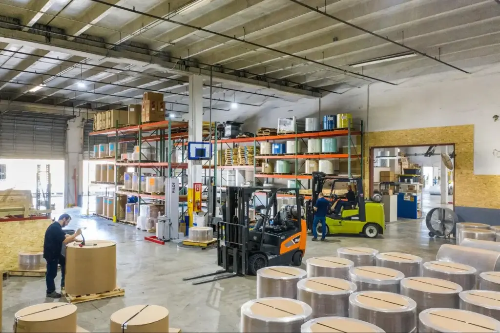 Warehouse workers in a loading operation featuring a combination of wooden pallets with bottom deck boards and wooden skids without bottom deck boards.
