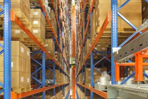 Robotic crane retrieving a palletized load from high-density vertical racking inside an automated storage and retrieval system warehouse.
